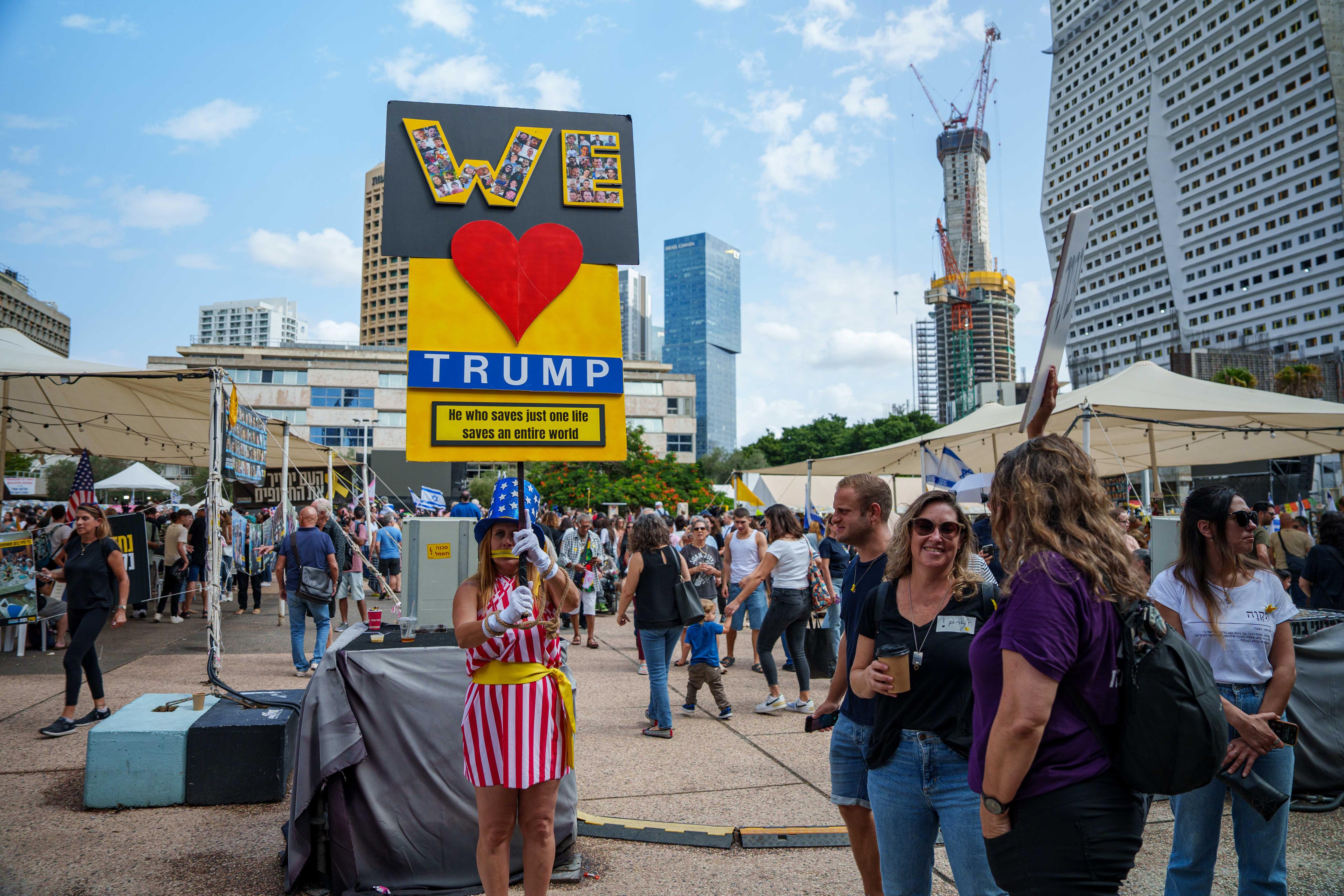 A woman wearing an outfit with the colours of the american flag and holding up a sign saying we love trump
