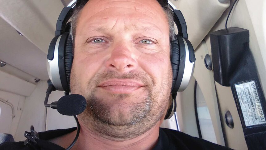 A man sits in the cockpit of a plane wearing headphones.