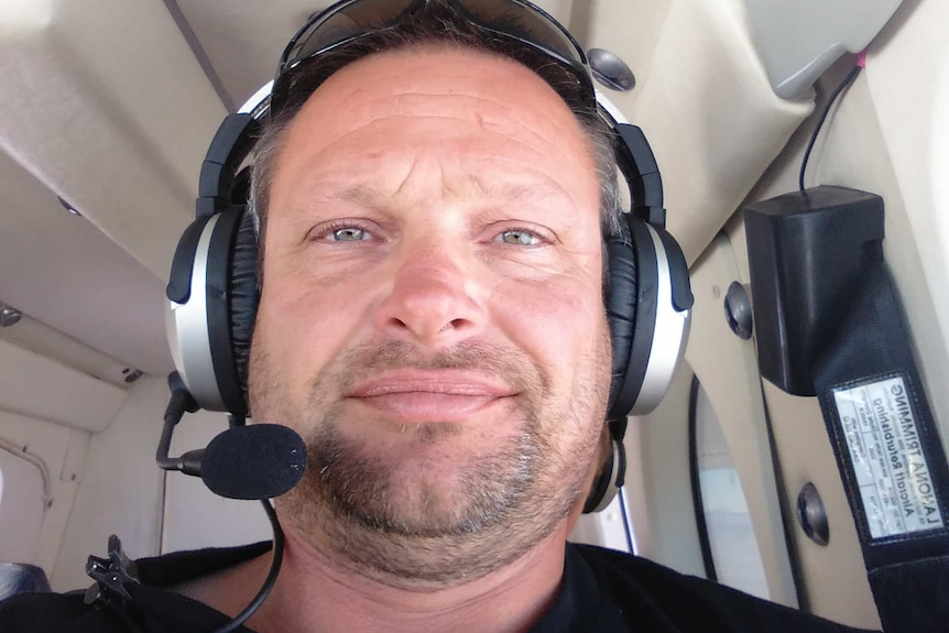 A man sits in the cockpit of a plane wearing headphones.