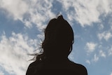  a woman with long hair silhouetted against a blue sky with white clouds