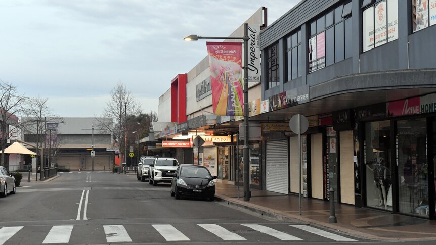 An empty street in the Sydney suburb of Fairfield, with only a few cars parked alongside some shops