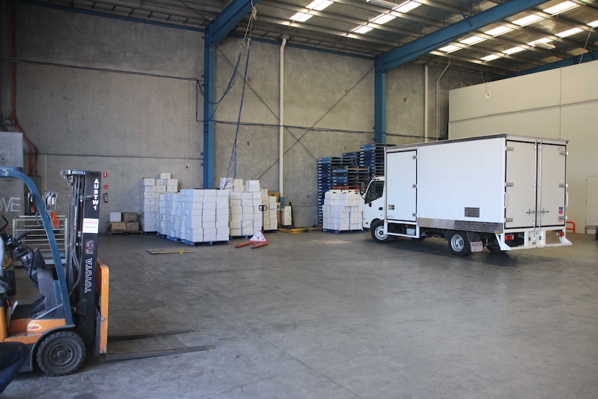 A truck in a warehouse with several stacked white boxes.