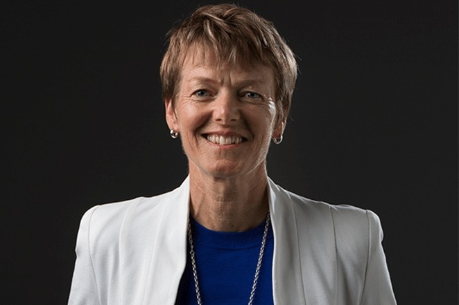 A woman with a blue shirt wearing a white jacket smiles at the camera 