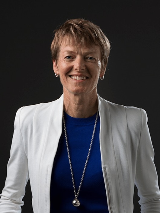 A woman with a blue shirt wearing a white jacket smiles at the camera 