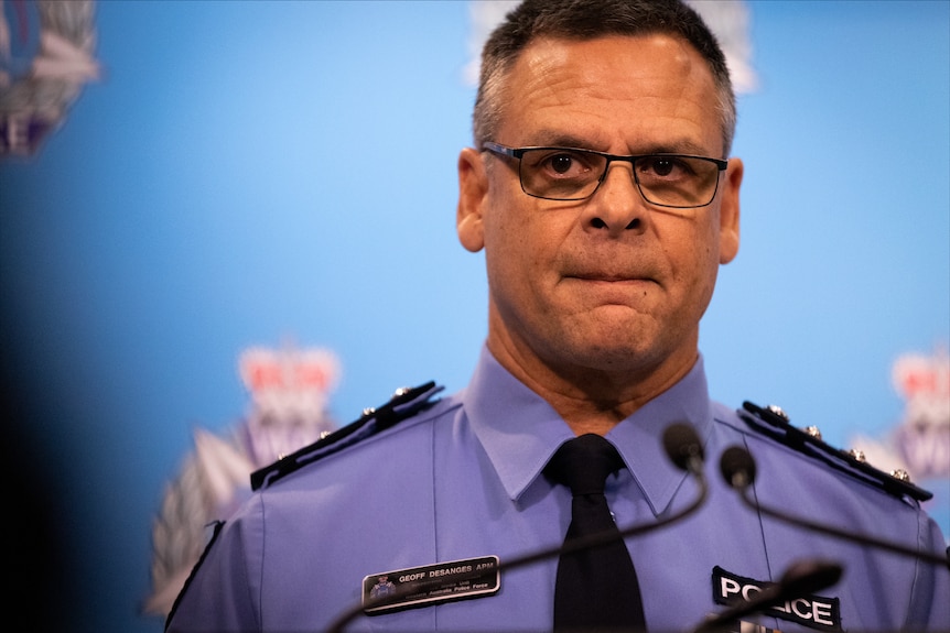 A tight medium close-up shot of WA Police Inspector Geoff DeSanges in uniform in front of a blue backdrop with his lips pursed.