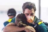 Pat Cummins wears a mask as he hugs his partner at an airport