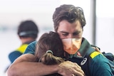 Pat Cummins wears a mask as he hugs his partner at an airport