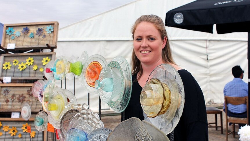 A woman stands with garden ornaments made from glass plates and vases.