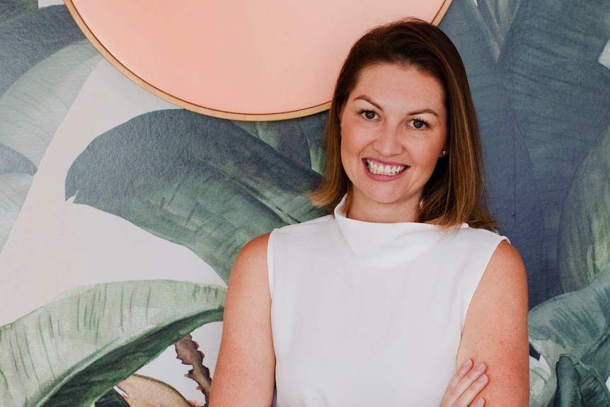 Woman with short brown hair and brown eyes smiles for a portrait against tropical wallpaper.