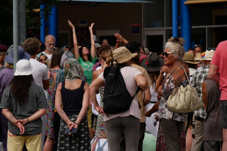 A large group of people not wearing masks. One woman has her hands up praying.