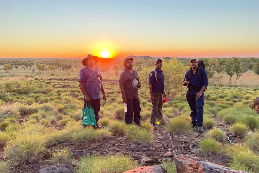 Four men standing near a sunrise in bushland. 