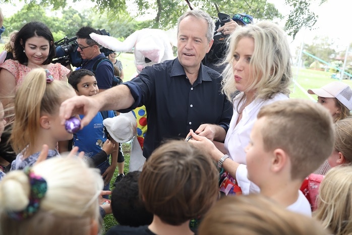 Bill Shorten hands an Easter egg to a group of children with his wife Chloe standing next to him.