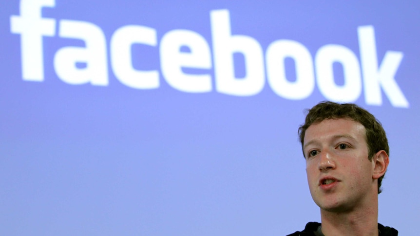 Mark Zuckerberg speaks with a Facebook logo on a screen behind him.