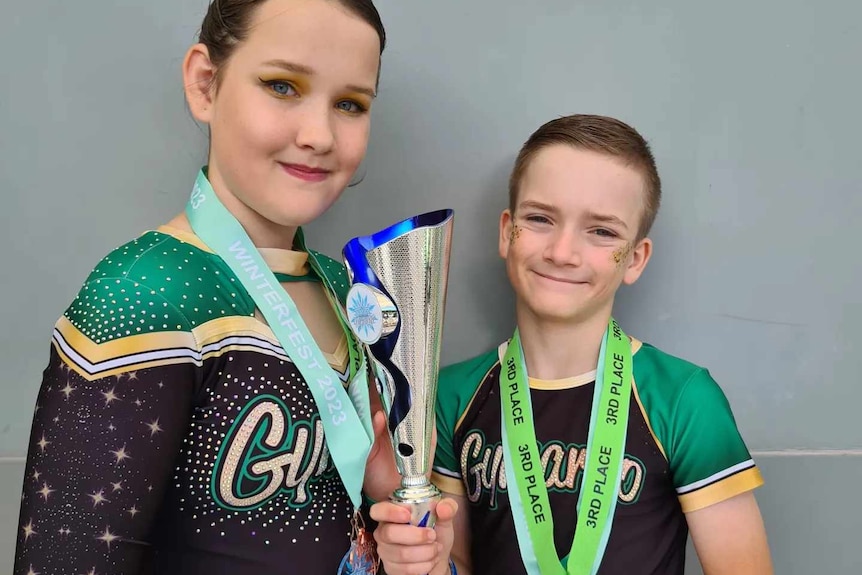 Girl and boy holding trophy in their green and black sports lycra uniform