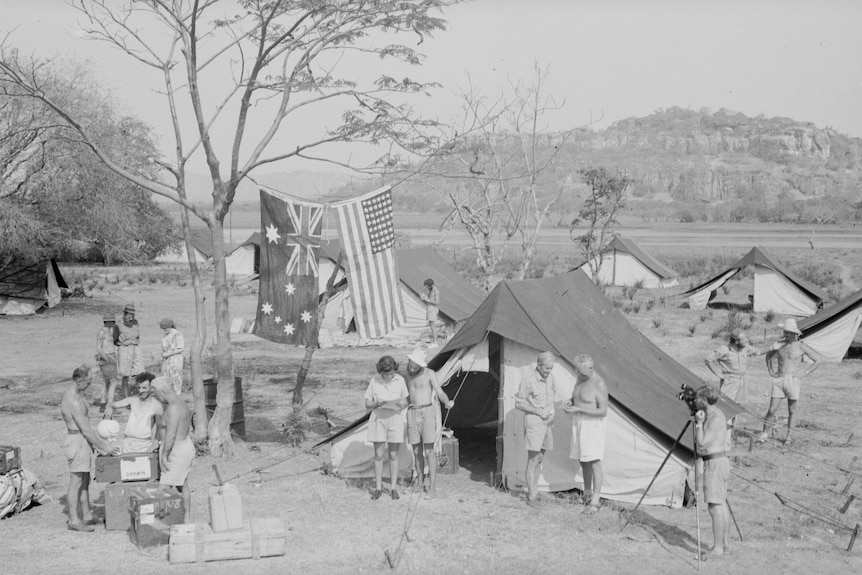 Une photo en noir et blanc de tentes dans l'arrière-pays avec des drapeaux australiens et américains suspendus à un arbre