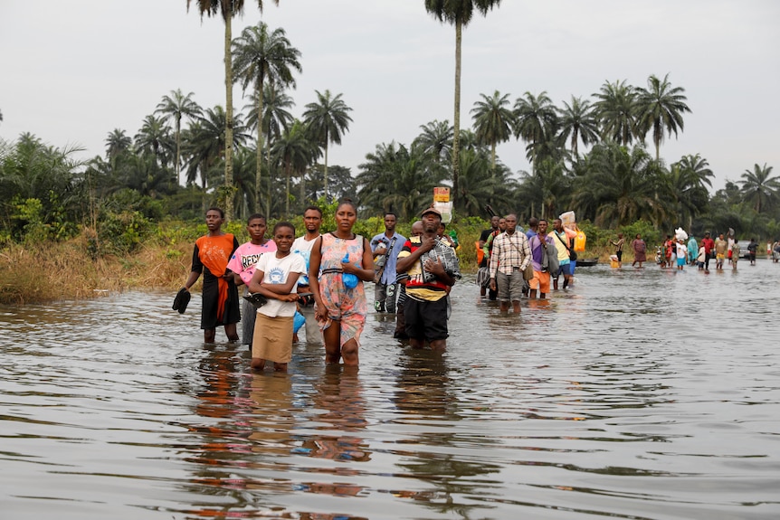 Nigerian men, women and children walk through knee-deep water while carrying possessions.