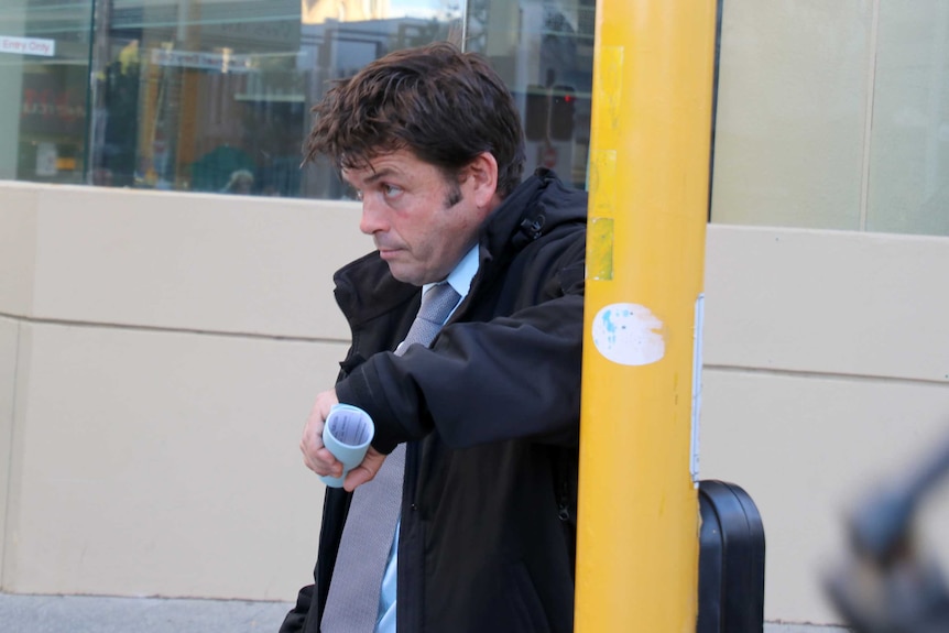 Matthew Kenny leans against a traffic light pole as he waits to cross the road.