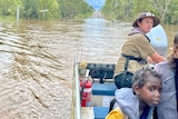 Three people drive atop flood waters on a road in Katherine.