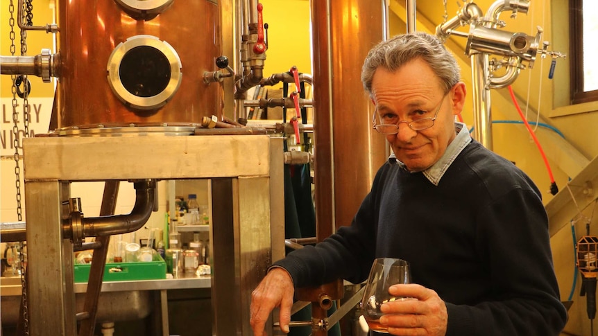 Phillip Moore, owner of Distillery Botanica, standing in front of a bronze gin distilling machine.