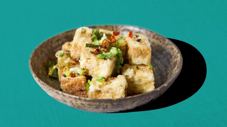 A bowl with salt and pepper tofu, garnished with chilli and shallots in a story about how to cook tofu properly.