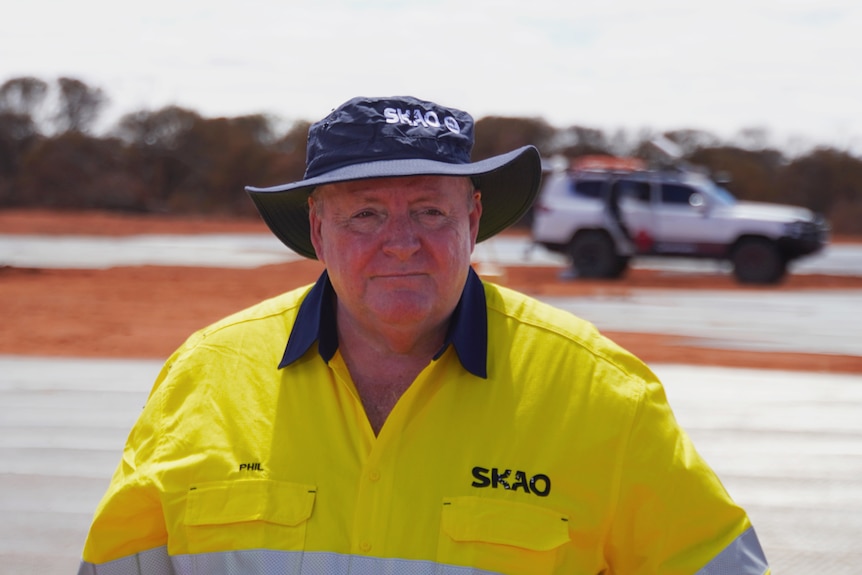 Philip Diamond in a high-vis shirt and a blue bucket hat, standing at the radio telescope site in the outback. 
