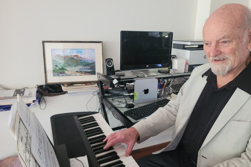 John Bath playing a tune on his keyboard with his watercolour painting in the background. 