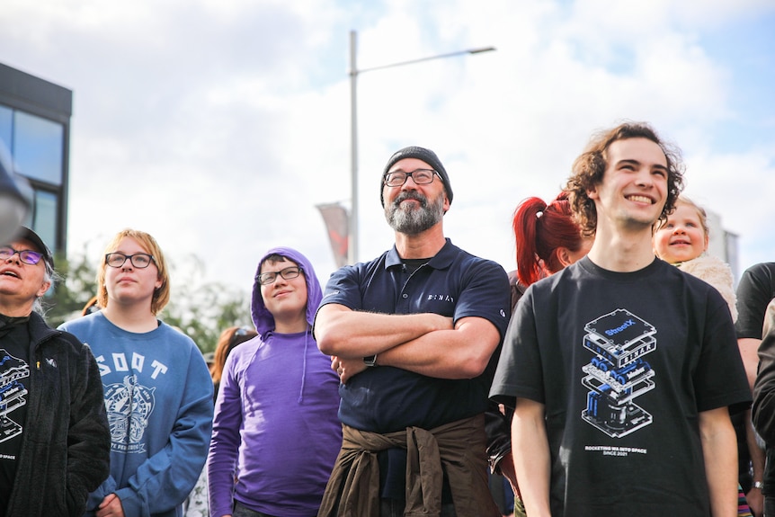 A group of people smiling and watching a screen outdoors