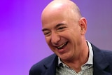 Jeff Bezos grins, crinkling the corners of his eyes as he glances down