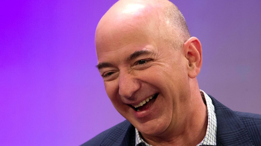 Jeff Bezos grins, crinkling the corners of his eyes as he glances down