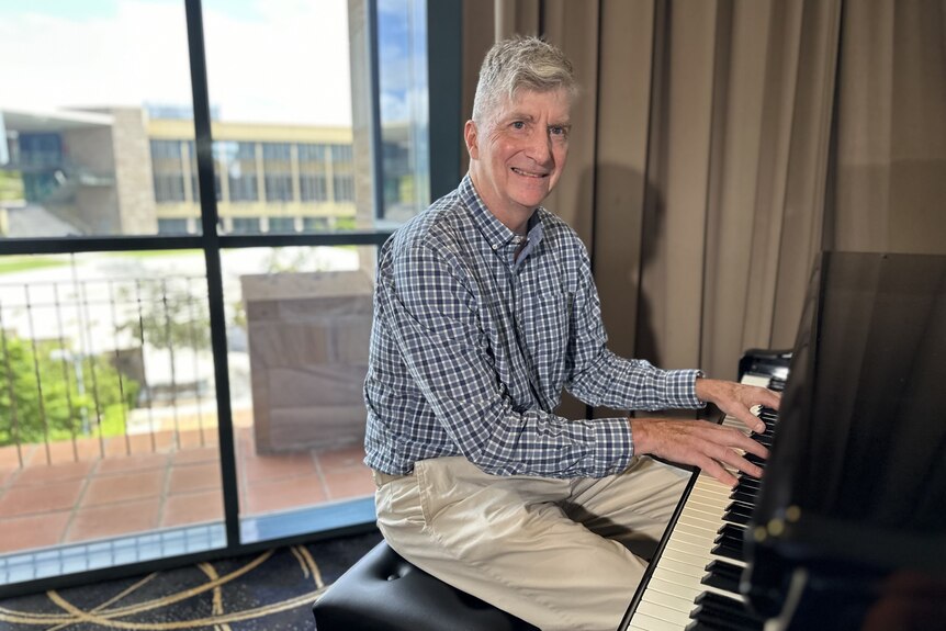 A smiling, middle-aged man plays a pino.