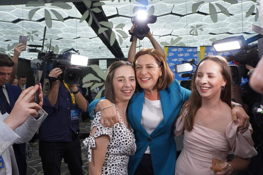 A woman hugs her daughters with cameras around her.