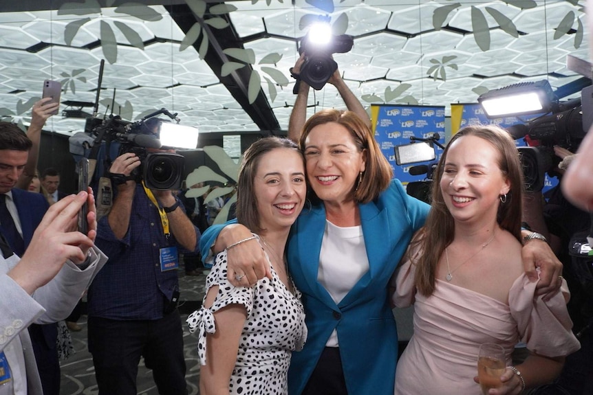 A woman hugs her daughters with cameras around her.