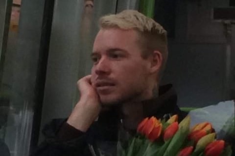 A blonde man sits on a bus holding a bunch of tulips