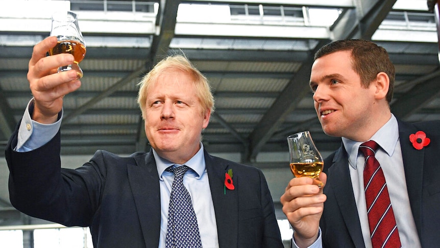 You look up at Boris Johnson alongside Douglas Ross who are holding up whiskey in stemmed glasses at a modern factory.