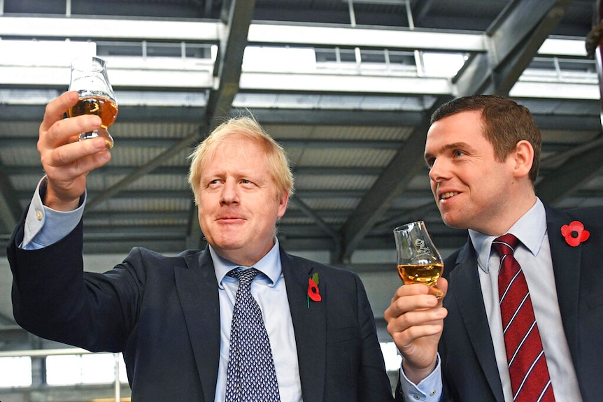 You look up at Boris Johnson alongside Douglas Ross who are holding up whiskey in stemmed glasses at a modern factory.