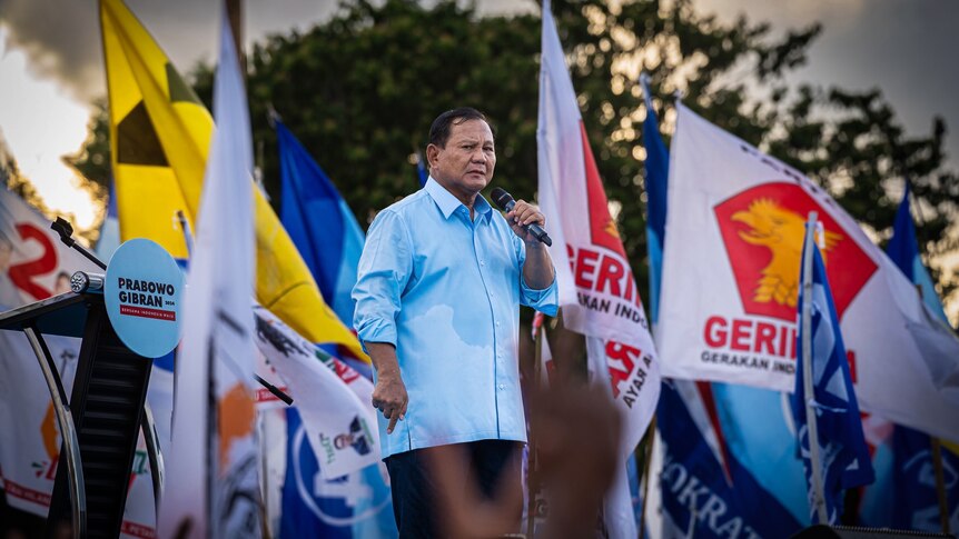 Prabowo Subianto looks into camera, sweat pooling in his armpits as he speaks into a microphone on stage