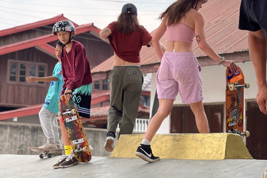 A group of people holding and on skateboards at the top of a concrete skate ramp