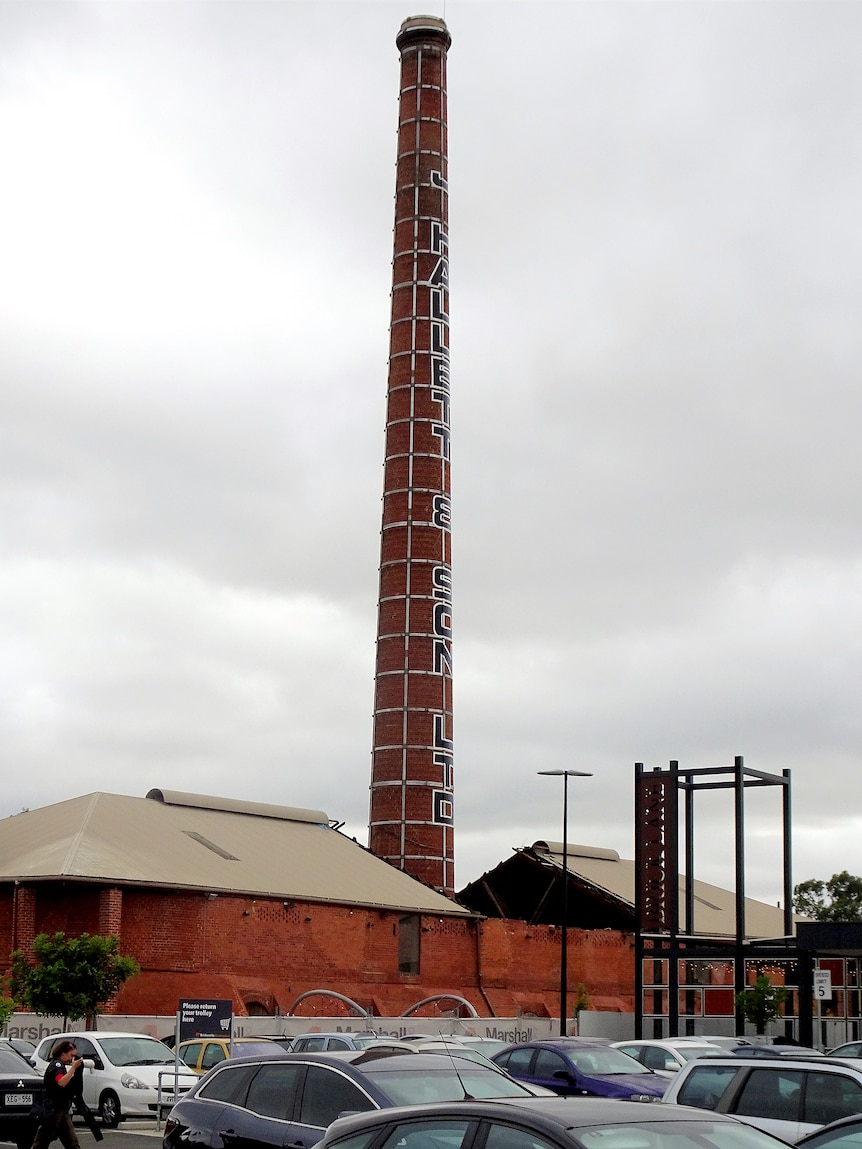 A very tall red brick kiln reaches to the sky from a building. 