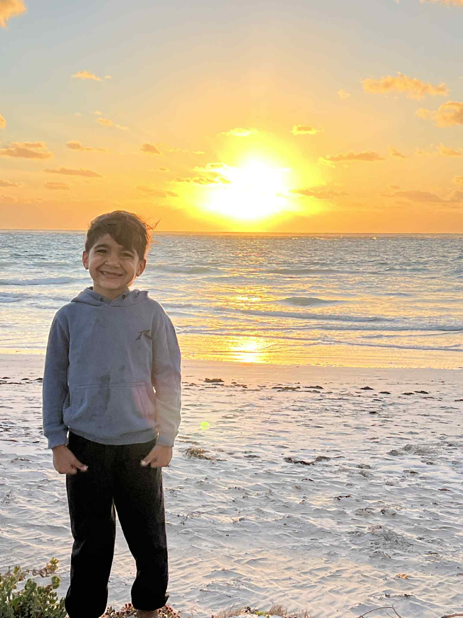 Un niño se encuentra en la playa al atardecer. 