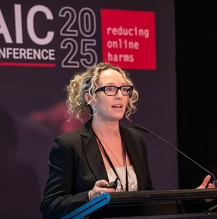 a blond woman stands at a lectern and delivers a speech into a microphone
