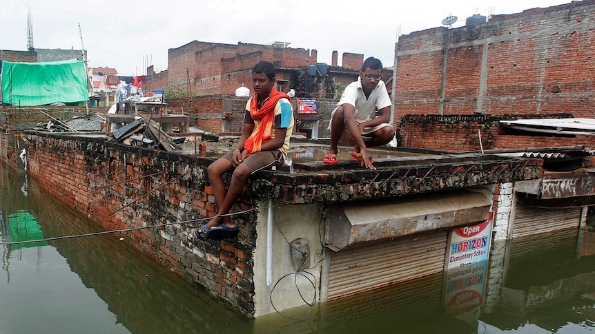 Men sit on the roof of a partially submerged shop.