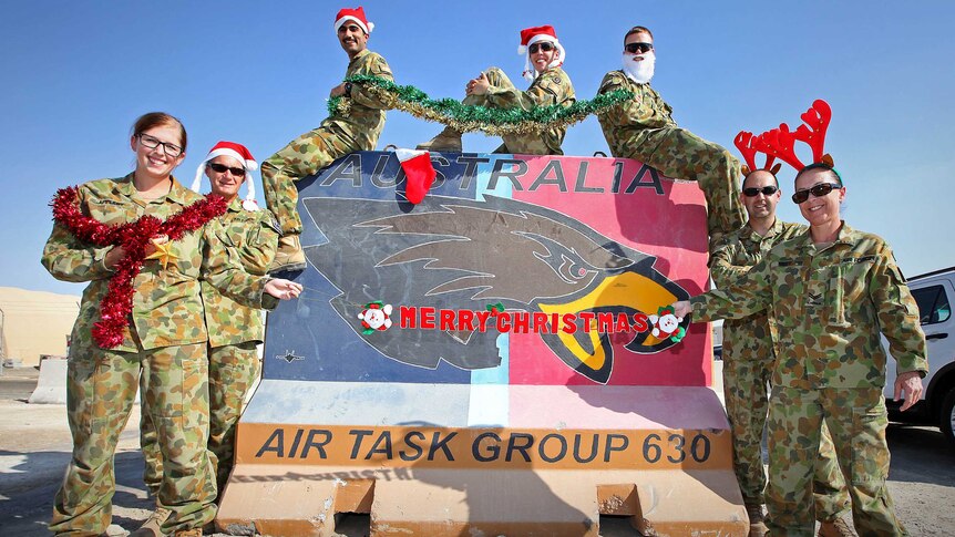 RAAF Logistics Cell personnel wearing Santa hats in front of sign at the Air Task Group Headquarters.