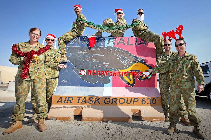 RAAF Logistics Cell personnel wearing Santa hats in front of sign at the Air Task Group Headquarters.