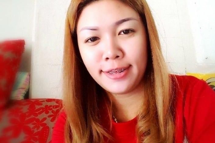 A close up of a woman with blonde hair, wearing a red shirt and smiling with braces.