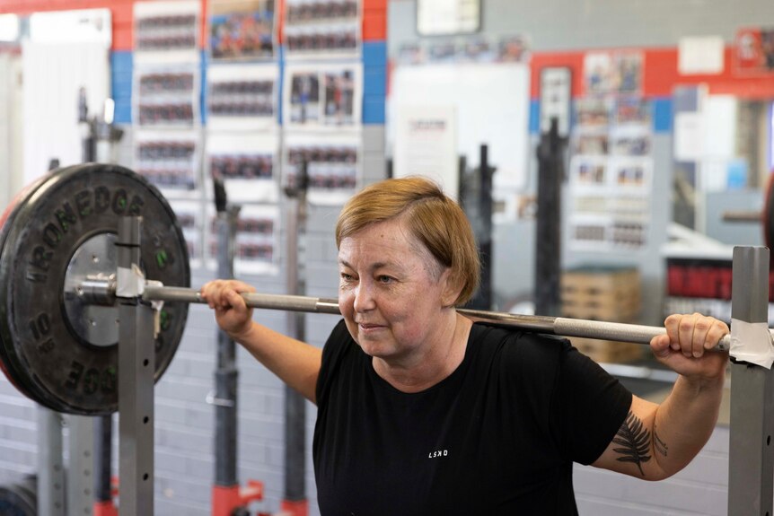 A middle-aged woman has weights on her shoulders and prepares to lift.