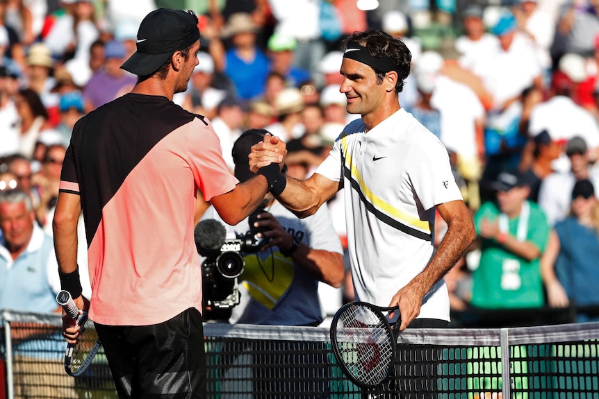Thanasi Kokkinakis shakes hands with Roger Federer at the net.