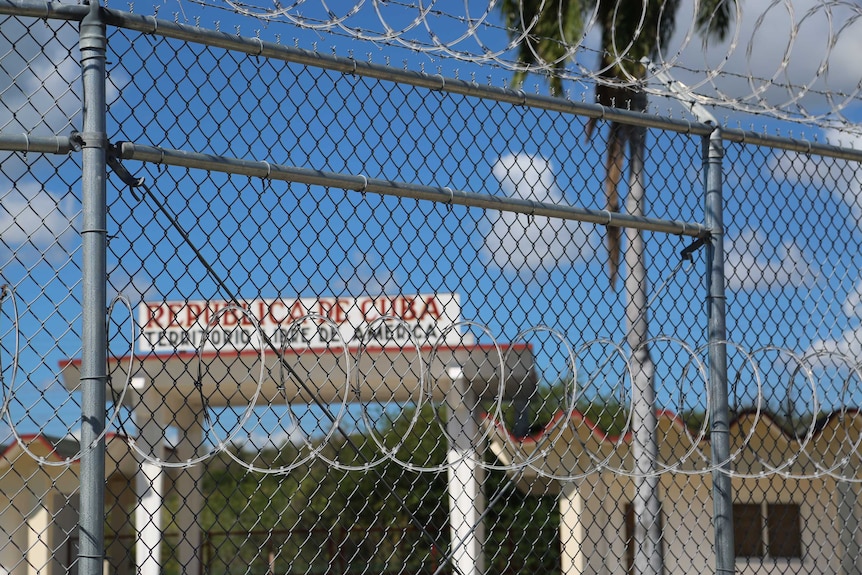 view through a chainlink fence with coils of razorwire to a sign saying "republica de cuba"