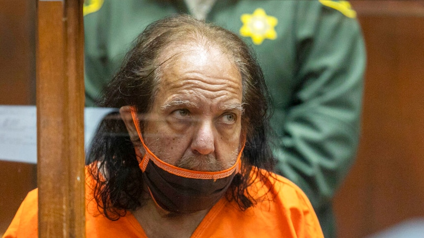 Ron Jeremy in orange prison clothes in court.