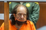 Ron Jeremy in orange prison clothes in court.