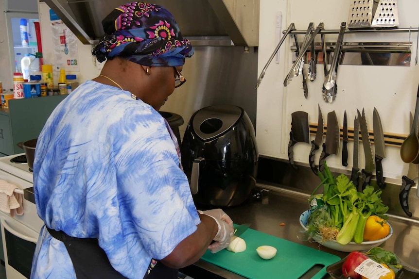 African woman in colourful turban chops up vegetables in cafe kitchen.